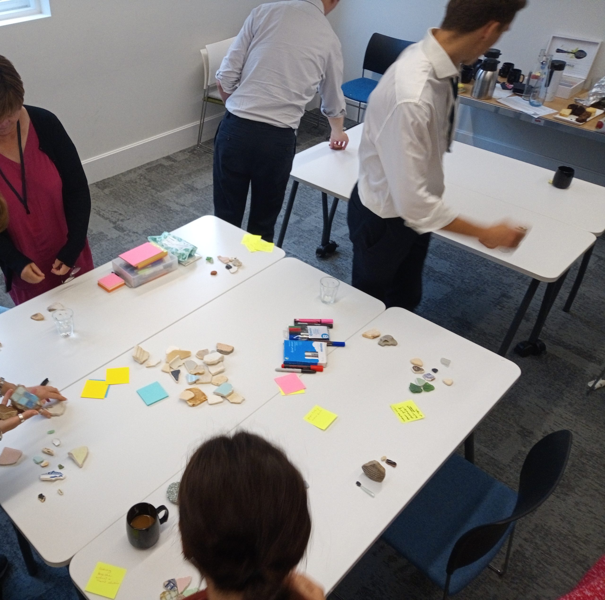 Workshop participants around a table with mosaic pieces, sticky notes and pens